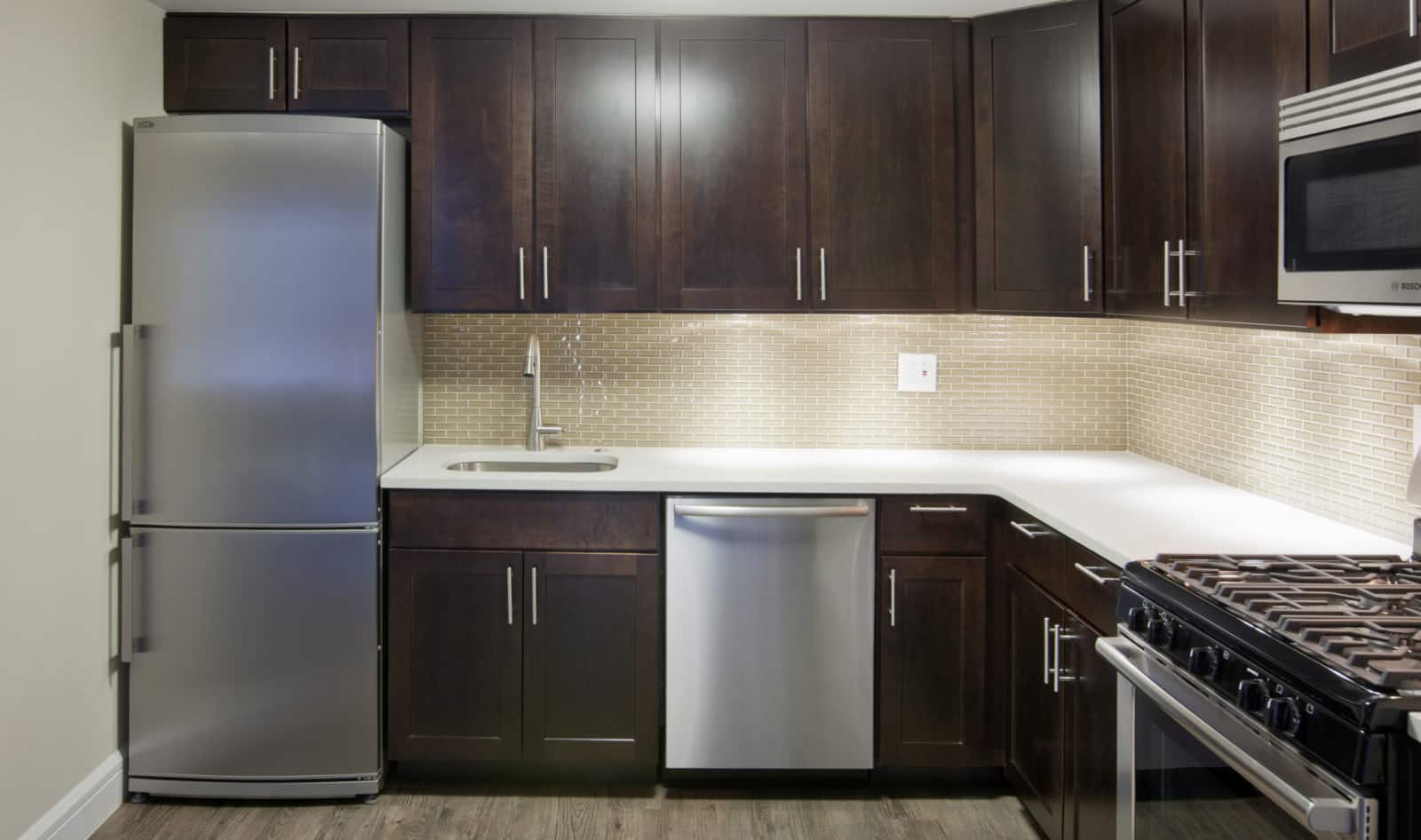 Interior of apartment kitchen with stainless steel appliances, white countertops and dark cabinets.