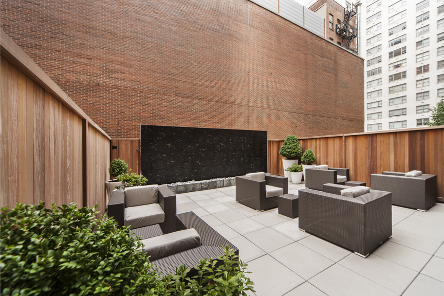 Exterior of outdoor courtyard with modern chairs, tables and a water feature in the background..