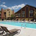 Outdoor pool area with lounge chairs and apartment building in the background.