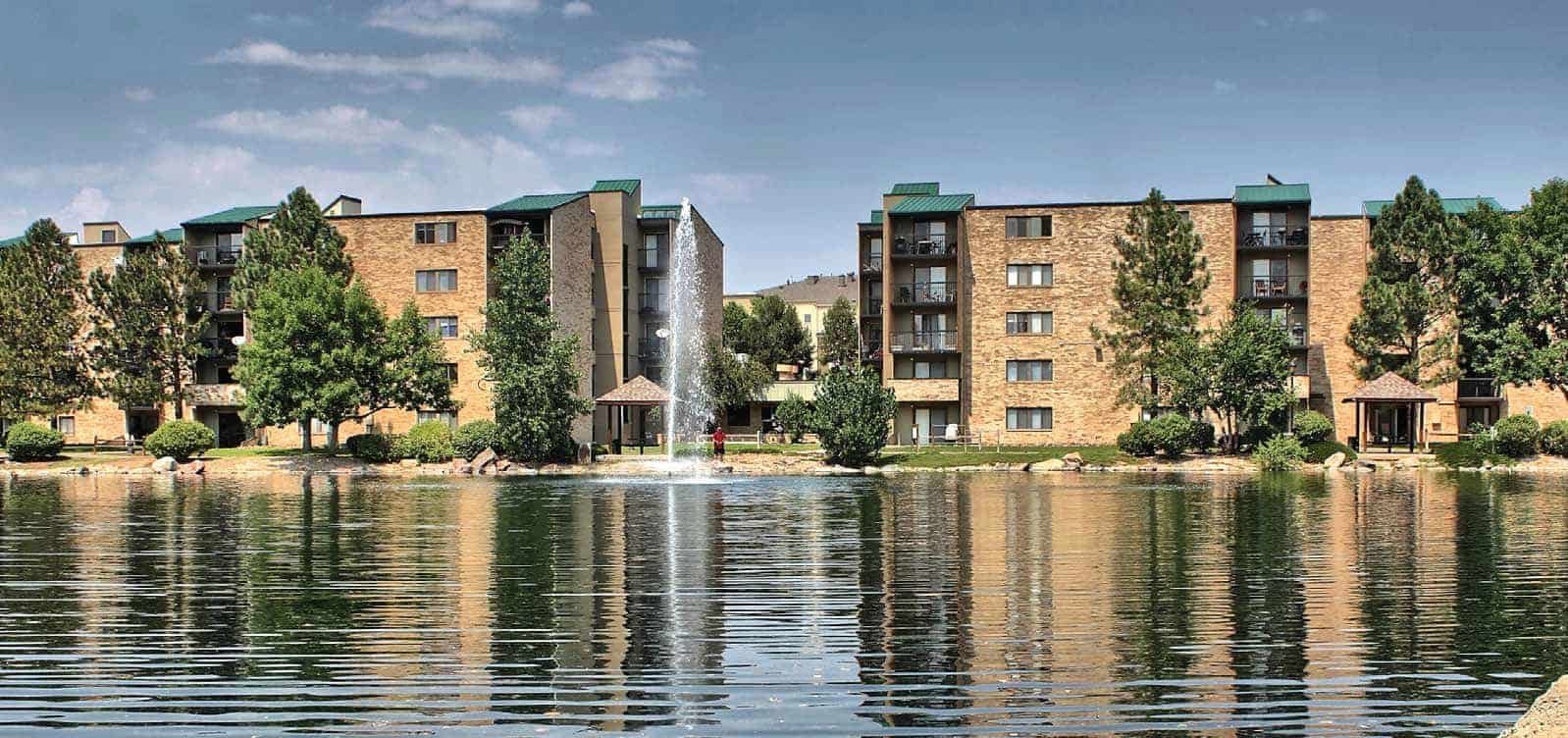 View of the lake and fountain with 5 story apartment buildings in the background.