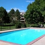 Outdoor pool surrounded by lawn and trees and apartment buildings.